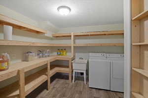 Clothes washing area with washer and clothes dryer, a textured ceiling, and hardwood / wood-style floors