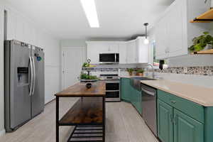 Kitchen featuring stainless steel appliances, pendant lighting, wood counters, white cabinets, and green cabinets