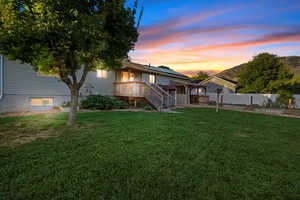 Back house at dusk featuring a yard and a wooden deck