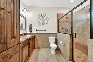 Bathroom featuring a shower with door, dual vanity, toilet, tile patterned flooring, and tile walls