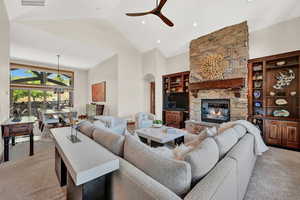 Living room with ceiling fan, built in shelves, light colored carpet, high vaulted ceiling, and a fireplace