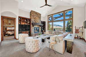 Carpeted living room with ceiling fan, high vaulted ceiling, and a fireplace