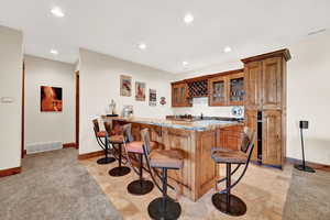 Kitchen featuring light tile patterned flooring, kitchen peninsula, a kitchen bar, and light stone counters