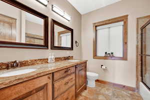 Full bathroom featuring tile patterned floors, double sink vanity, shower / bath combination with glass door, and toilet