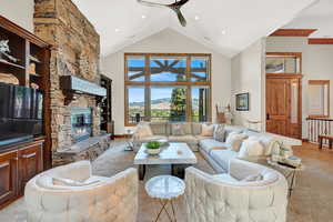 Tiled living room featuring ceiling fan, high vaulted ceiling, and a stone fireplace