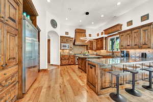 Kitchen featuring custom range hood, light hardwood / wood-style floors, built in appliances, and tasteful backsplash