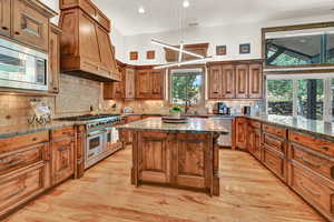 Kitchen featuring appliances with stainless steel finishes, custom range hood, light wood-type flooring, and backsplash