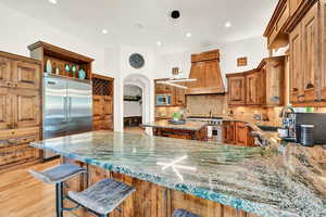 Kitchen featuring light wood-type flooring, decorative backsplash, built in appliances, custom range hood, and light stone countertops