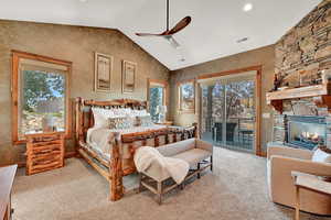 Carpeted bedroom with access to exterior, vaulted ceiling, a stone fireplace, and multiple windows