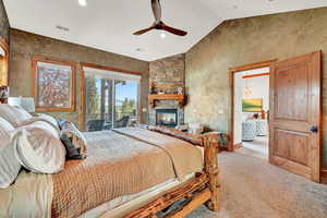 Carpeted bedroom featuring a fireplace, access to outside, ceiling fan with notable chandelier, and lofted ceiling