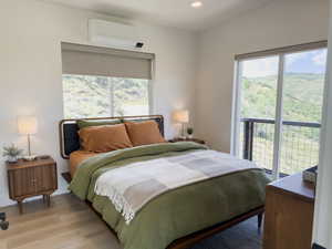 Bedroom featuring a wall mounted AC, multiple windows, light hardwood / wood-style floors, and access to exterior