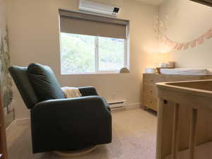 Living area with baseboard heating, a wall mounted air conditioner, and light colored carpet