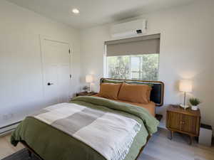 Bedroom with a wall mounted AC and light wood-type flooring