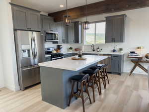 Kitchen with hanging light fixtures, light hardwood / wood-style floors, beamed ceiling, stainless steel appliances, and sink