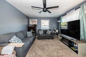 Carpeted living room featuring ceiling fan and a textured ceiling