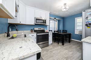 Kitchen featuring sink, appliances with stainless steel finishes, light stone countertops, cooling unit, and white cabinetry