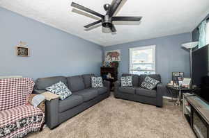 Living room featuring a textured ceiling, ceiling fan, and light carpet