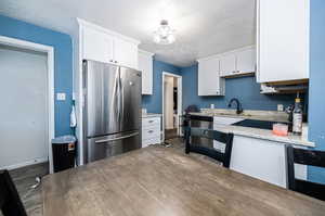 Kitchen featuring white cabinetry, sink, light stone counters, stainless steel fridge, and dark wood-type flooring