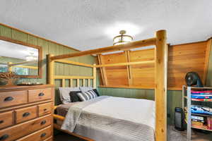 Carpeted bedroom featuring a textured ceiling and wooden walls