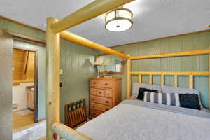 Bedroom with wood walls, hardwood / wood-style flooring, baseboard heating, a textured ceiling, and ensuite bathroom