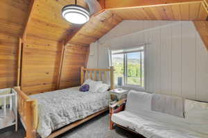 Carpeted bedroom featuring wood ceiling, wooden walls, and lofted ceiling with beams