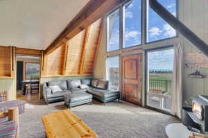 Living room with high vaulted ceiling, beam ceiling, a wood stove, carpet floors, and a textured ceiling