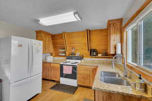 Kitchen featuring a wealth of natural light, sink, light wood-type flooring, white appliances, and light stone countertops