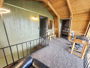 Interior space with wood ceiling, carpet floors, lofted ceiling with beams, and wood walls