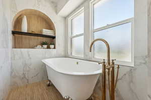 Bathroom featuring a wealth of natural light, a bathing tub, and tile walls