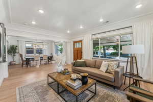 Living room featuring light wood-type flooring, an inviting chandelier, and ornamental molding