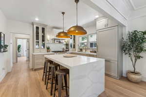 Kitchen featuring light wood-type flooring, a kitchen island, hanging light fixtures, light stone countertops, and sink