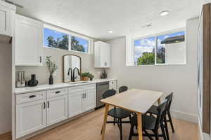 Kitchen with light hardwood / wood-style floors, stainless steel dishwasher, and white cabinetry