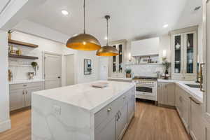 Kitchen featuring decorative light fixtures, light hardwood / wood-style flooring, range with two ovens, a kitchen island, and gray cabinetry