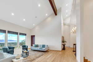 Living room featuring beamed ceiling, light hardwood / wood-style flooring, high vaulted ceiling, and an inviting chandelier