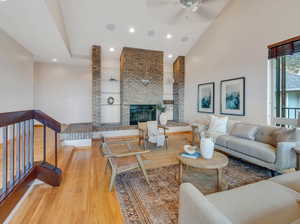 Living room featuring light hardwood / wood-style flooring, ceiling fan, brick wall, a fireplace, and high vaulted ceiling