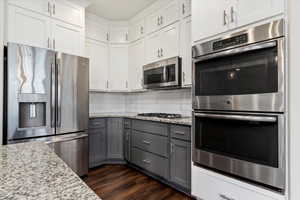 Kitchen featuring appliances with stainless steel finishes, dark wood-type flooring, tasteful backsplash, gray cabinets, and white cabinets