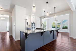 Kitchen with a kitchen breakfast bar, dark wood-type flooring, white cabinets, light stone countertops, and double oven