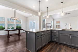 Kitchen featuring decorative light fixtures, dark wood-type flooring, lofted ceiling, and light stone countertops