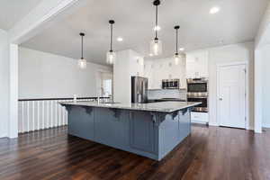 Kitchen with dark hardwood / wood-style floors, tasteful backsplash, a kitchen bar, appliances with stainless steel finishes, and light stone counters