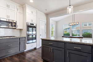 Kitchen with appliances with stainless steel finishes, decorative backsplash, white cabinetry, dark hardwood / wood-style floors, and lofted ceiling