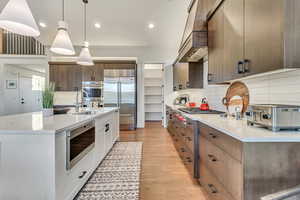 Kitchen featuring custom range hood, light hardwood / wood-style flooring, appliances with stainless steel finishes, tasteful backsplash, and sink