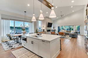 Kitchen featuring sink, decorative light fixtures, light hardwood / wood-style floors, a center island with sink, and white cabinets