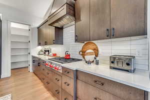 Kitchen with premium range hood, tasteful backsplash, stainless steel gas stovetop, light hardwood / wood-style floors, and lofted ceiling