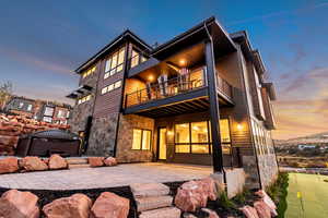 Back house at dusk featuring a balcony and a patio