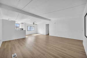 Unfurnished living room with beam ceiling, ceiling fan, and light wood-type flooring