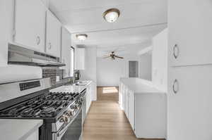 Kitchen with stainless steel gas stove, sink, light wood-type flooring, white cabinets, and ceiling fan