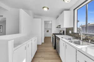 Kitchen with backsplash, sink, light hardwood / wood-style floors, white cabinets, and lofted ceiling