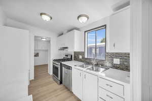 Kitchen with sink, light hardwood / wood-style floors, dishwasher, white cabinetry, and lofted ceiling