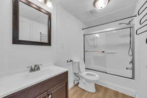 Full bathroom featuring hardwood / wood-style floors, toilet, shower / bath combination with glass door, and vanity