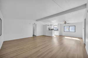 Unfurnished living room with ceiling fan, beam ceiling, and light hardwood / wood-style flooring